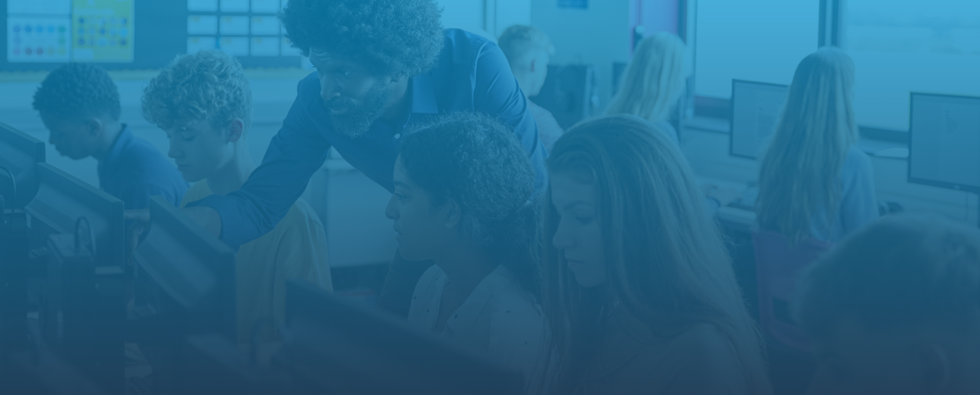 A teacher helping students work together in a computer classroom